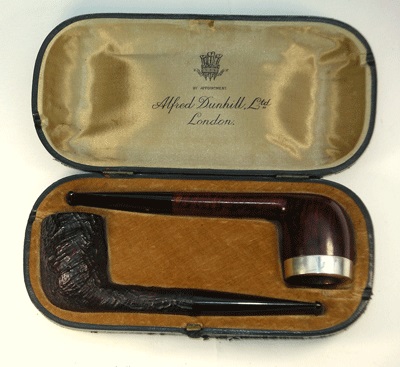 A vintage tobacco pipe set displayed in an open case, featuring a dark brown carved pipe and a polished pipe with a silver band, branded 'Alfred Dunhill Ltd, London'.