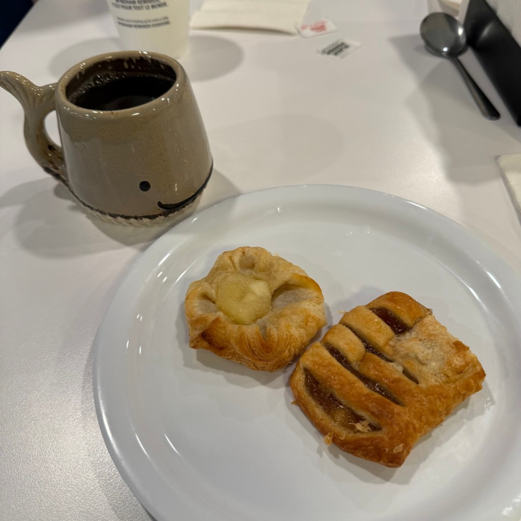 A ceramic mug of black coffee next to a plate containing two pastries: one with a creamy filling and another with a fruit filling.