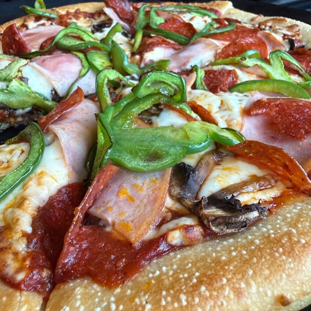 Close-up of a pizza topped with mozzarella cheese, sliced ham, pepperoni, mushrooms, and green bell peppers.