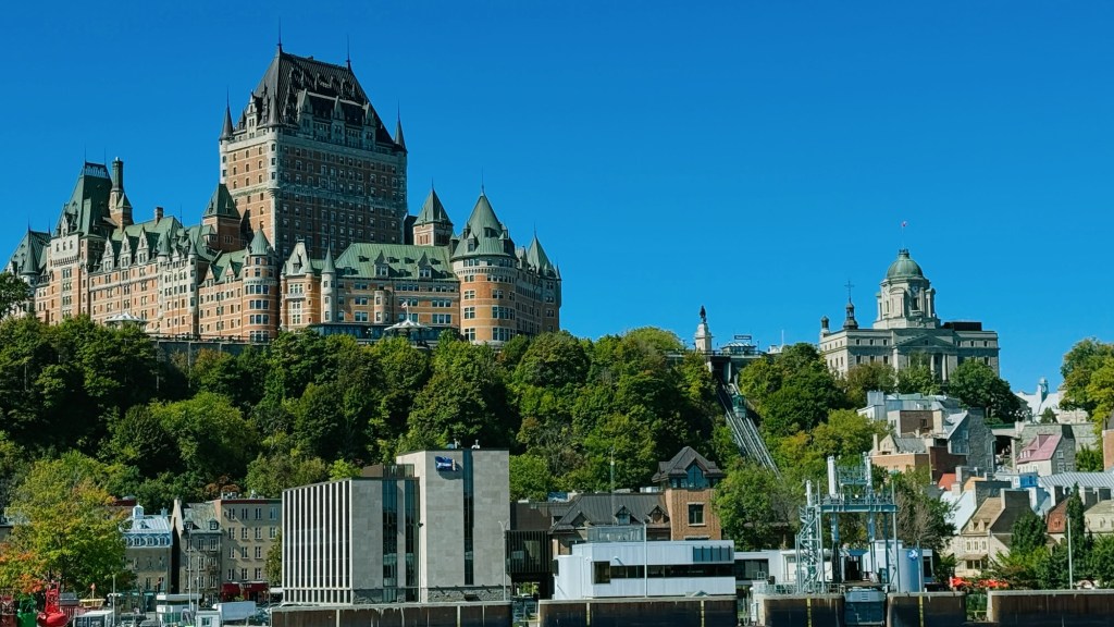Historic Château Frontenac overlooking the St. Lawrence River, surrounded by greenery and city buildings under a clear blue sky.